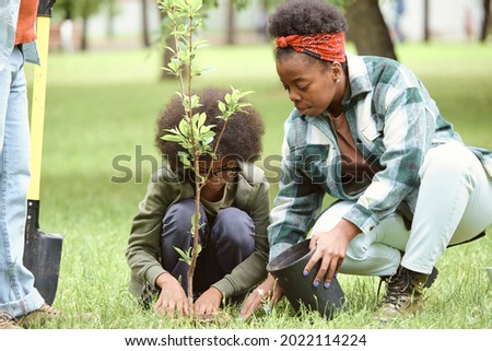 Young female and her little son planting tree in one of city parks on summer day Royalty-Free Stock Photo #2022114224