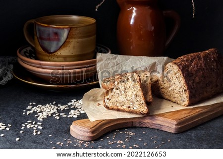 Bread with sunflower and flax seeds on a wooden cutting board. Ceramic crockery in the background.