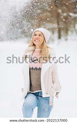 Happy blond woman plays with a snow in winter day. Girl enjoys winter, frosty day. Playing with snow on winter holidays, a woman throws white, loose snow into the air. Walk in winter forest.