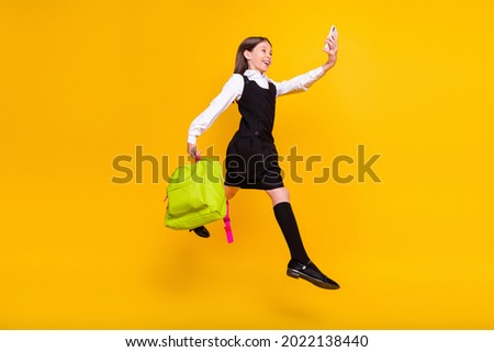 Full length body size photo schoolgirl jumping with schoolbag taking selfie isolated bright yellow color background