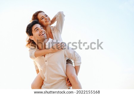 Young satisfied fun happy enamored smiling couple two friends family man woman in casual clothes boyfriend give piggyback ride to joyful girlfriend sit on back look aside on light white sky background Royalty-Free Stock Photo #2022155168
