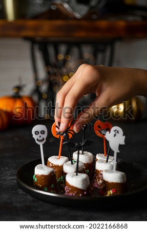  Sweet Halloween treat, chocolate covered marshmallows with sugar and Halloween decorations on a black plate, vertical photo with soft focus