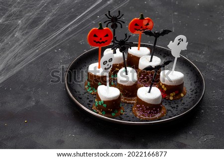  Sweet Halloween treat, chocolate covered marshmallows with sugar and Halloween decorations on a black plate, photo with soft focus and free space for text