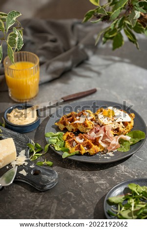 Savory vegetable waffles with cheese, egg, orange juice on grey textured table - beautiful healthy diet breakfast. Farm country concept. Copy space. Homemade pastry. Sunny light.