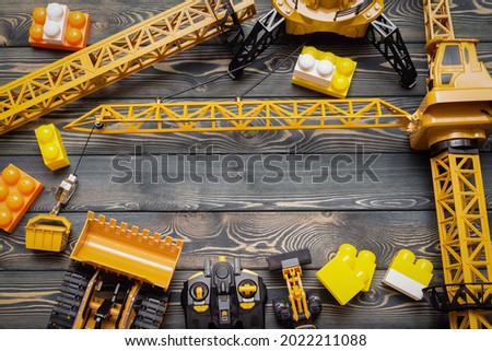 Yellow construction crane, bulldozer toy and control joypad on the wooden flat lay table background.