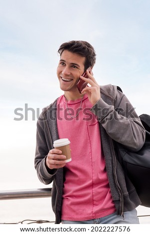 vertical photo of a happy student with a coffee laughing while talking by mobile phone outdoors, concept of technology of communication and urban lifestyle, copy space for text