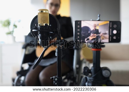 Woman is recording video of playing the guitar while sitting in wheelchair