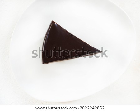 Top view of a slice of brownie chocolate cake or pie in a white plate on a white wooden background.