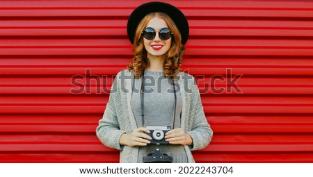 Portrait of young woman photographer with vintage film camera on a red background