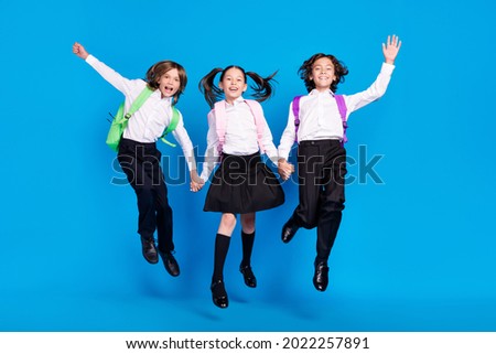 Photo of pretty adorable schoolchildren wear uniform rucksacks jumping high holding arms smiling isolated blue color background Royalty-Free Stock Photo #2022257891