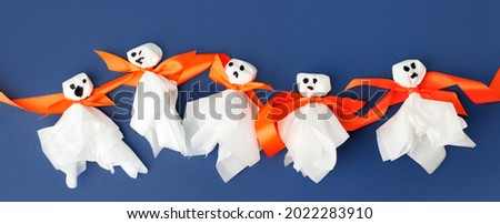 Making paper garland with ghost Home for Halloween party. Easy crafts for kids. DIY creative idea, Flat lay on blue background. Handcrafted decorations, daycare, kindergarten, preschool