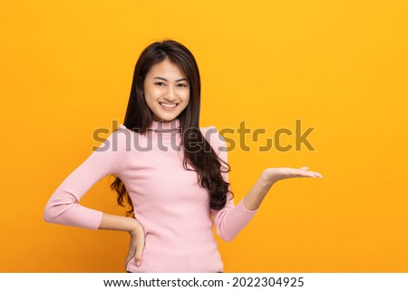 Attractive Beautiful asian woman open hands palm up holding something. Surprised happy female on isolated yellow background. Thai teenage girl around 20. Royalty-Free Stock Photo #2022304925