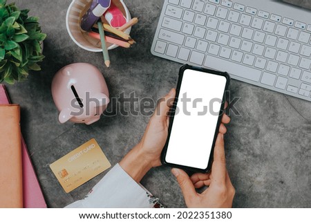 Top view, Woman hands using smartphone with mock-up blank screen display on desk.	
