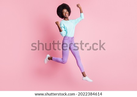 Full length photo of lucky cute dark skin lady wear colorful clothes rising fists jumping high isolated pink color background