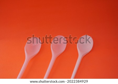 Stock photo of 3 stacks of white plastic spoons lined up and neatly arranged so that it looks aesthetic. Isolated on an orange background. Cutlery industry, design, website photos.
