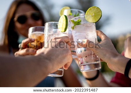 Group of young people clinking cocktail drink glasses toasting. Best friends wearing a lowered face mask having a funny reunion. Royalty-Free Stock Photo #2022391487