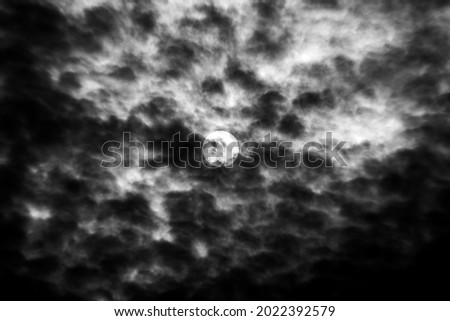 black and white photograph of sun behind clouds