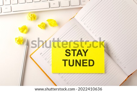 STAY TUNED text on sticker on diary with keyboard and pencil