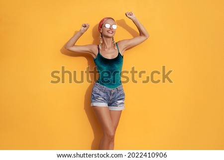 Happines and summer vacation. Young excited woman with rised hands against yellow wall.