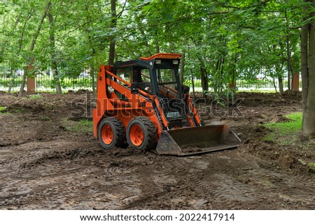 Skid steer loader clearing the site in public park moving soil and performing landscaping works for the territory improvement. Royalty-Free Stock Photo #2022417914