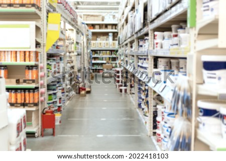 Blurred aisle and shelves with building and finishing materials in hardware store. View of hypermarket rows with paints. Shopping and trading background. Royalty-Free Stock Photo #2022418103