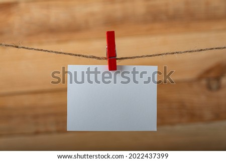 Blank white note card hanging with clothespin on rope string peg. Vertical frame.