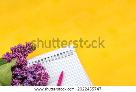 Notebook lilacs on yellow background. Spiral notebook and pen. Notepad with pen and flowers.