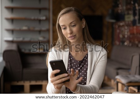 Focused positive young business woman making call on cellphone, using online app and services on cell, holding device, looking at screen, reading, browsing, chatting, texting, shopping. Gadget addict