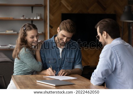 Happy millennial couple signing property purchase contract, insurance agreement, filling bank application for mortgage, buying house, loan. Young married man and woman meeting with legal expert Royalty-Free Stock Photo #2022462050