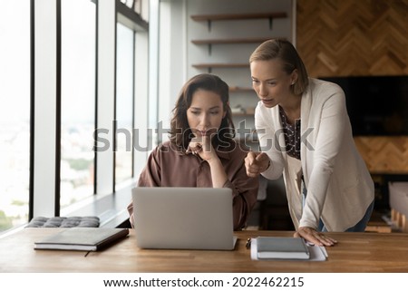 Corporate mentor supervising work of intern, giving help and professional advice, training skills of new employee. Managers meeting at laptop, discussing content on screen, talking. Teamwork concept Royalty-Free Stock Photo #2022462215