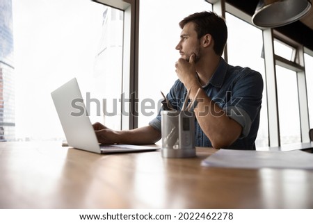 Thoughtful employee, business man, manager looking out of window in deep thought, sitting at workplace with laptop in office, thinking over company future, pondering on decision for work task Royalty-Free Stock Photo #2022462278