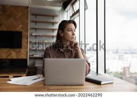 Thoughtful business owner woman looking out of window at city, sitting at workplace with laptop, thinking over solutions, challenges, company future vision, making decision, feeling uncertain Royalty-Free Stock Photo #2022462290