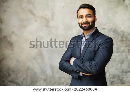 Smiling middle-age Indian high skilled leader in formal suit looks at the camera, confident ambitious bearded arabic businessman stands in office with arms folded on the grey background Royalty-Free Stock Photo #2022468884