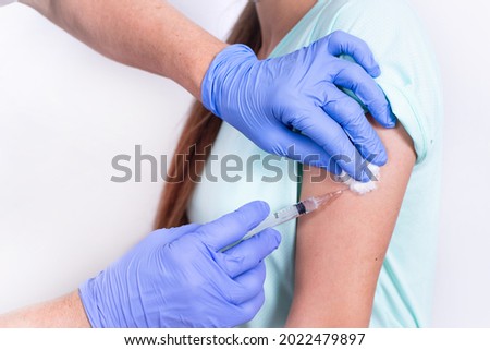 Female doctor or nurse giving shot or vaccine to patient's shoulder - young girl. Close-up. Vaccination against flu, pandemic coronavirus. Mandatory prevention of people for immunity from the virus.