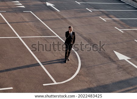 Top view of man in formalwear talking on mobile phone while standing on parking lot with arrow sign on it