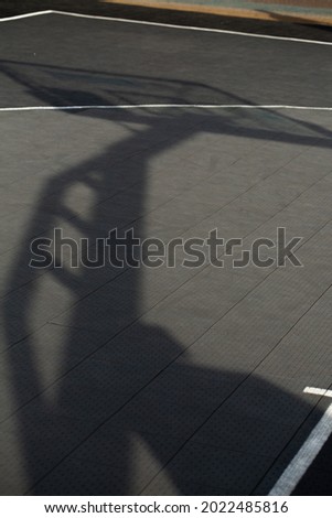 Photo of the shadow of a basketball hoop on grey basketball court during the day