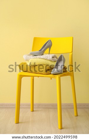 Chair with stack of stylish clothes and female shoes near color wall