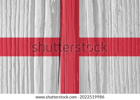 The flag of England on a dry wooden surface, cracked with age. It seems to flutter in the wind. Background, wallpaper or backdrop with national symbol. Saint George's Cross. Hard sunlight with shadows