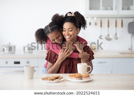 Emotional black daughter teenager hugging her beautiful happy mom while enjoying cookies, homemade pastry and biscuits together at home, kitchen interior. Family lifestyle, motherhood, parenthood Royalty-Free Stock Photo #2022524651