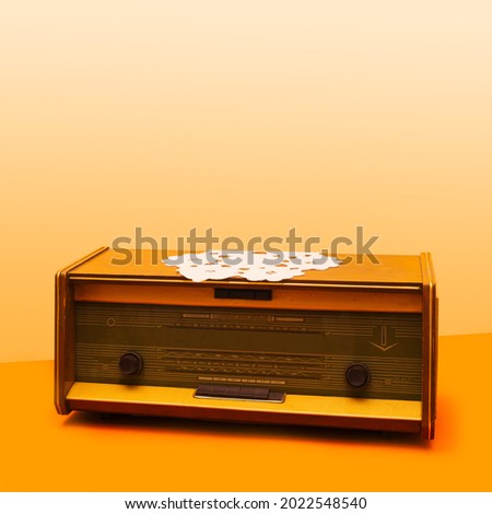An antique radio with unique vintage crochet cloth table on it. Old school arrangement against beige and light orange background.