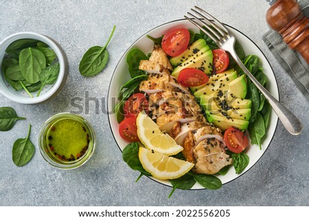 Fresh green salad with grilled chicken fillet, spinach, tomatoes, avocado, lemon and black sesame seeds with olive oil in white bowl on light slate background. Diet Concept. Top view copy space Royalty-Free Stock Photo #2022556205