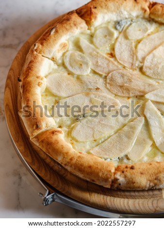 Pizza with white sauce, pear and cheese mix - mozzarella, parmesan, camembert, blue cheese and gorgonzola on traditional Italian bread dough backed in oven. Closeup, selective focus.