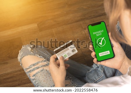 Businesswoman paying her bills with smartphone and credit card. Mobile phone with payment sent inscription screen and credit card in hand. Work from home concept photo