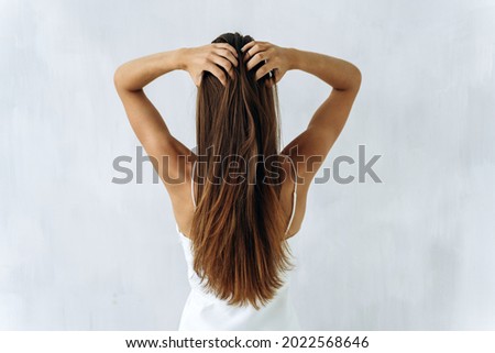 Beauty and care of hair. Waist up back side portrait of young brunette lady with straighten voluminous hair touching to it with her hands. Isolated on white 