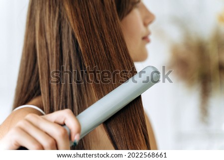 Hairdressing. Woman with beautiful long straight hair using hair straightener. Gorgeous girl straightening healthy hair with flat iron. Hair ironing and hairstyle concept  Royalty-Free Stock Photo #2022568661