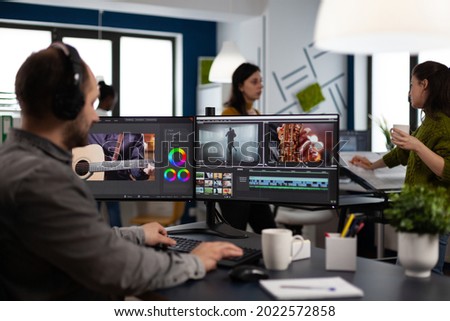 Videographer listening music on headphones editing creative movie using post production software working in business multimedia agency office. Artist man processing audio film montage on computer