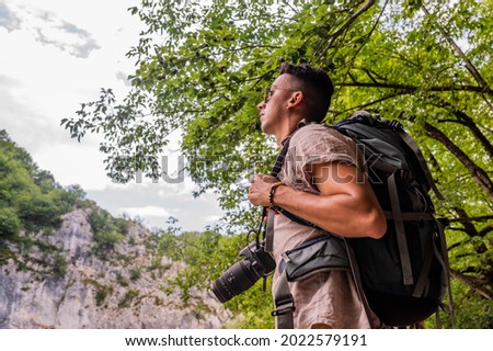 Young Brazilian man with a camera looking thoughtfully towards the mountains in Plitvice Lakes National Park, Croatia