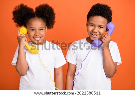 Photo of little funny girl boy talk telephone wear white t-shirt isolated on orange background