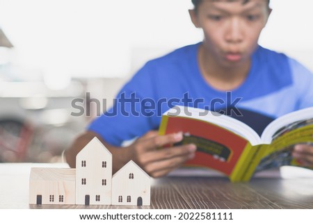 Asian man shows amazement while looking at a book, small wooden house model, home buying planning