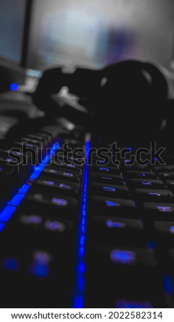 Keyboard with back lit keys close up with computer screen and headphones in background